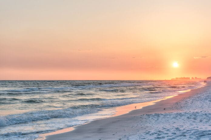 Dreamy pink peach orange sunset in Santa Rosa Beach, Florida with Pensacola coastline coast cityscape skyline in panhandle with ocean gulf mexico waves, birds